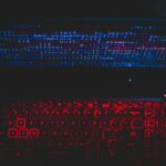 Dark-themed laptop setup with a red glowing keyboard and code on screen, ideal for tech enthusiasts.