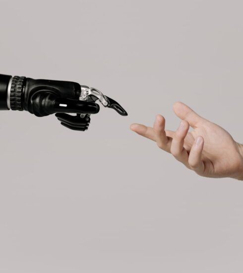 A human hand reaching to touch a bionic prosthetic hand on a white background.